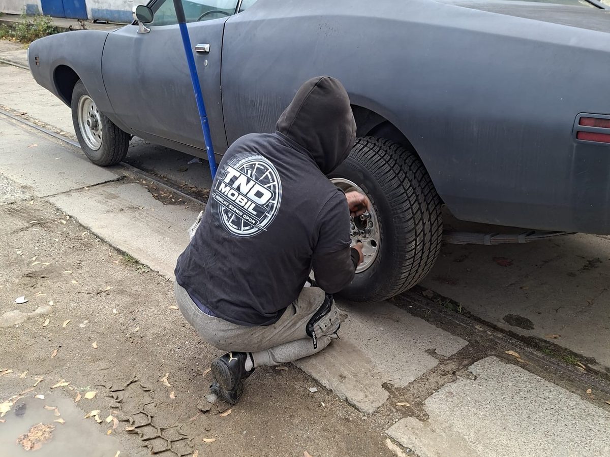 Technik TND Mobil w bluzie z logo zmienia koło u klienta